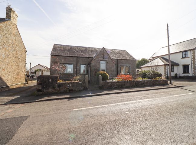 A stone house with a stone garden wall and plants in front at The Old School in Lowick