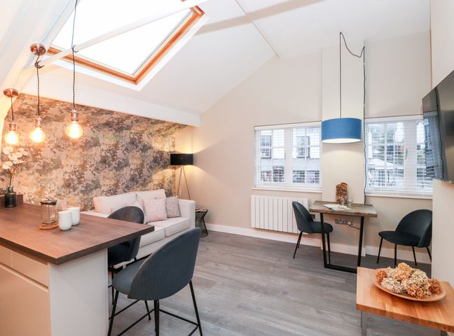 A living area with a sofa near a textured wall three hanging lights above a wooden counter two chairs at a small table under windows and a blue pendant light at Fenty's in Bowness-On-Windermere
