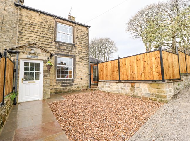 Stone cottage with gravel courtyard and wooden fence at April Cottage in Cross Hills