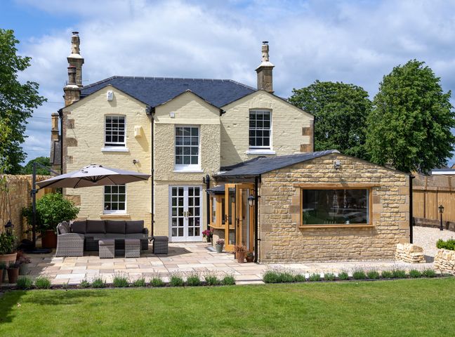 A backyard with patio furniture and umbrella next to a two-story house with stone extension at Cotsall House in Broadway