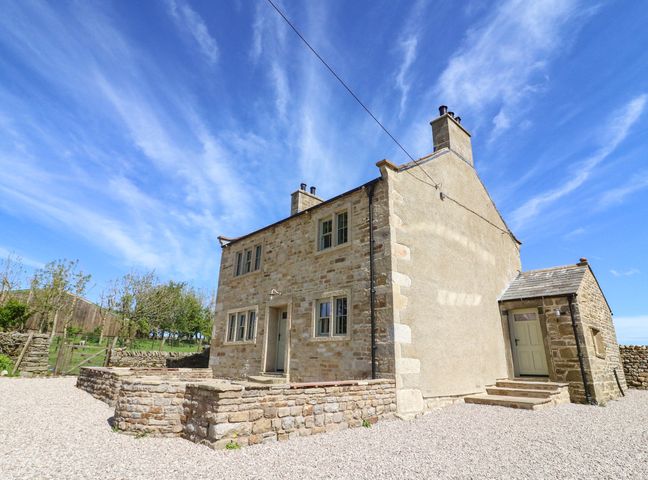 A stone house with multiple windows and chimneys under a blue sky at Lanshaw House in High Bentham
