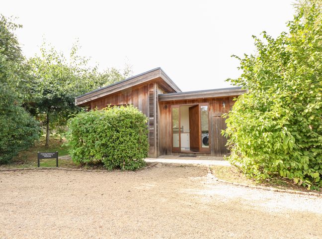 A wooden house with an open door surrounded by bushes and trees at Harleys House in Exton Rutland
