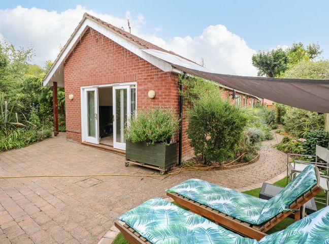 A brick house with sliding glass doors and a paved patio with lounge chairs and plants at Birch Cottage in Brundall