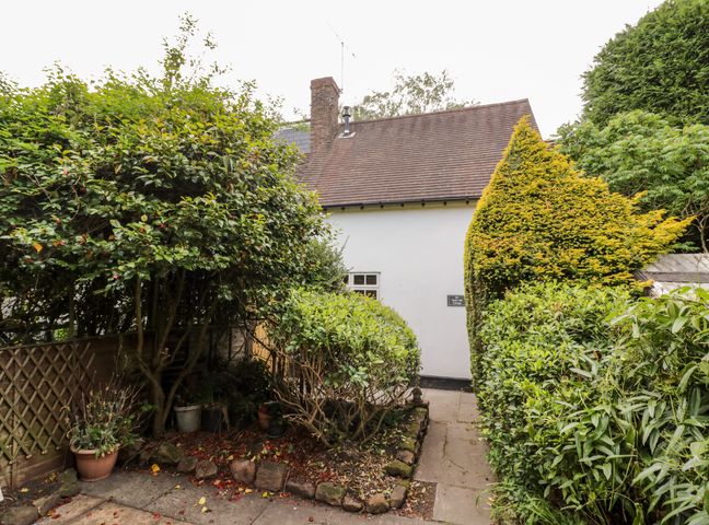 A pathway surrounded by bushes leading to a white building with a tiled roof at Hock-tide Cottage in Kenilworth