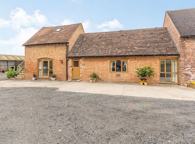 A brick building with multiple wooden doors and windows with plants outside at The Granary at Lane End Farm in Wickhamford near Broadway