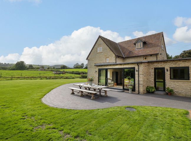 A stone house with a patio and outdoor table in a green field at Grove Farm in Cardington near Church Stretton