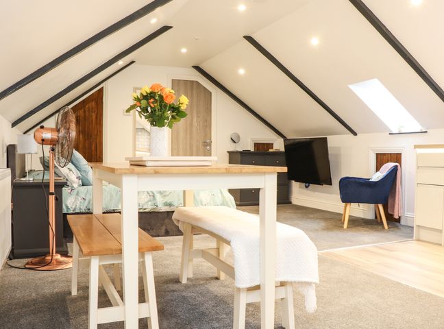 A loft bedroom with dining table bench flowers armchair and television at Thomas Chambers in Camborne