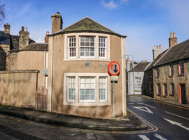 A street corner with beige buildings and a traffic sign showing priority for oncoming vehicles at The Toll House in Melrose