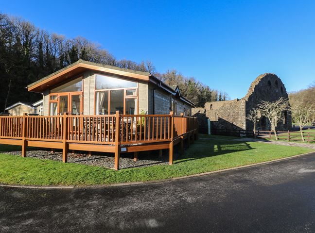 A single-story wooden cabin with a deck and railing next to stone ruins on grass at Seventh Heaven in Wisemans Bridge