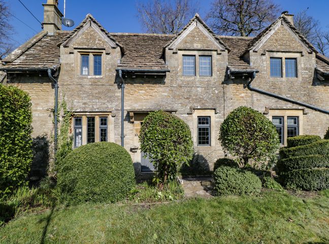Stone cottage with multiple windows and a tiled roof surrounded by trimmed bushes and grass at Rose Cottage in Corsham