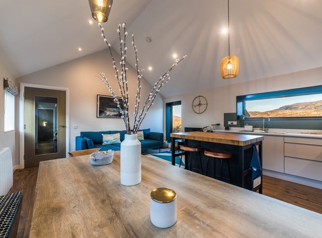 A kitchen and living area with a wooden table vase and blue sofa at Beinn Mhor View in Lochboisdale