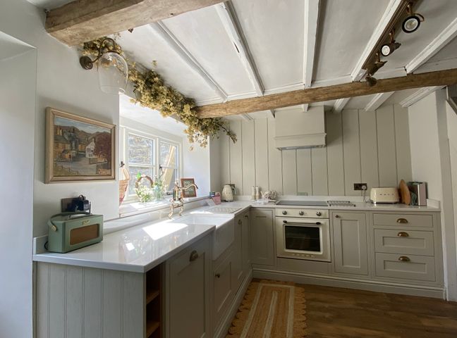A kitchen with cabinets oven sink and window with flowers at The Cottage on the Island in Castleton Peak District