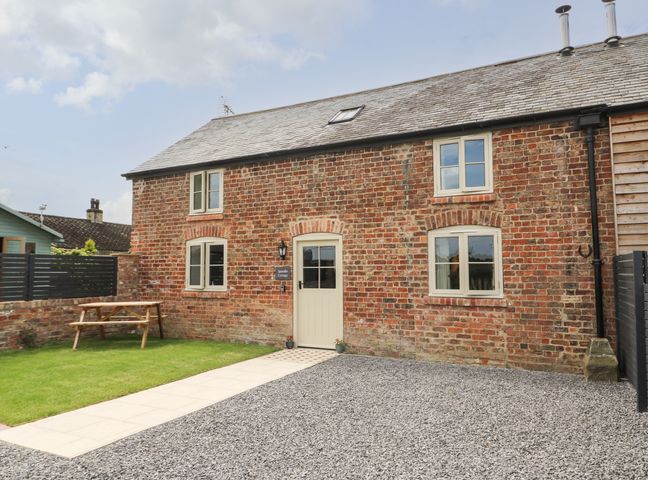A brick cottage with four windows a door a gravel driveway a paved path and a wooden picnic table at Spindle Cottage in Bielby near Seaton Ross