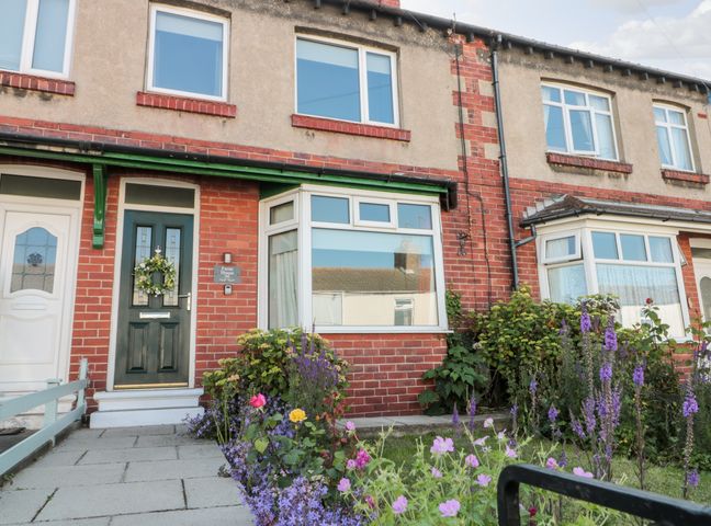 Front view of a brick terraced house with a green door and flower garden at Faran House in Staithes