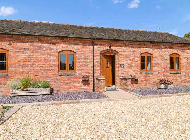 A brick building with four windows and a wooden door with stone steps and flower planters at Robins Rest in Blythe Bridge