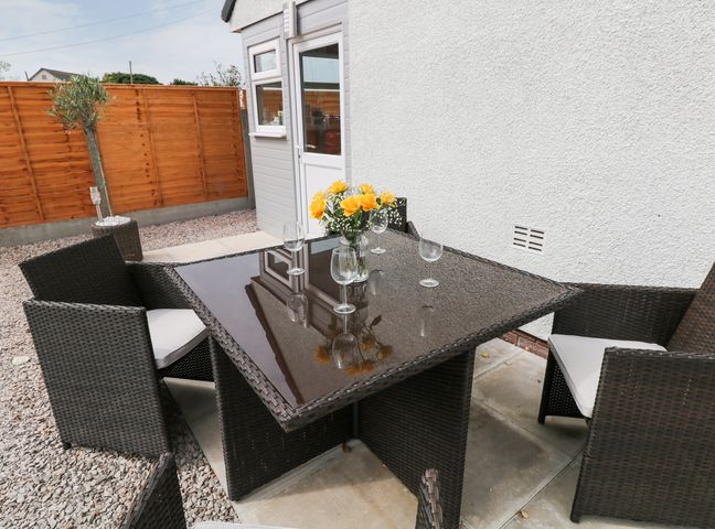 An outdoor patio area with a glass top table four wicker chairs and a vase with yellow flowers at White Stones in Goadsbarrow near Roose