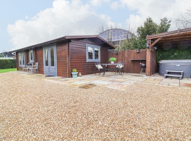 A wooden cabin with outdoor seating and a covered hot tub on a stone patio at Westfield Lodge in Terrington near Sheriff Hutton