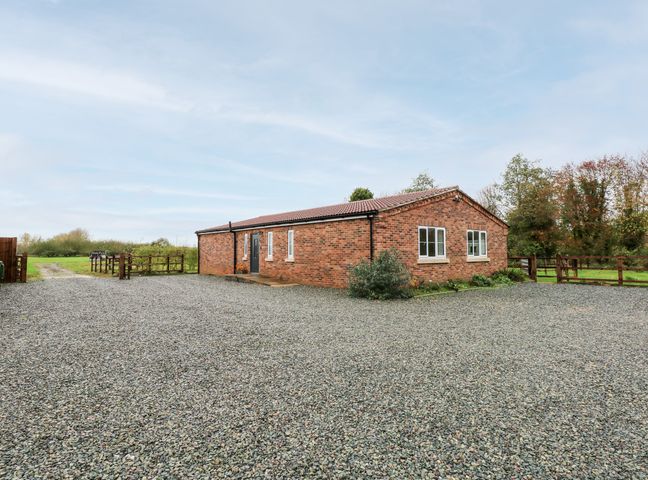 A single story brick house with a tiled roof surrounded by a gravel driveway and wooden fences at The Apple Shed in Wisbech