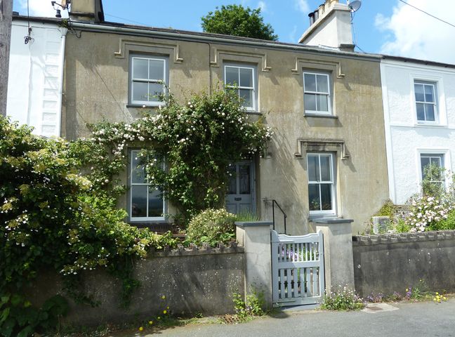 A two-story house with climbing plants and flowers around the entrance gate at Wenallt in Porthmadog