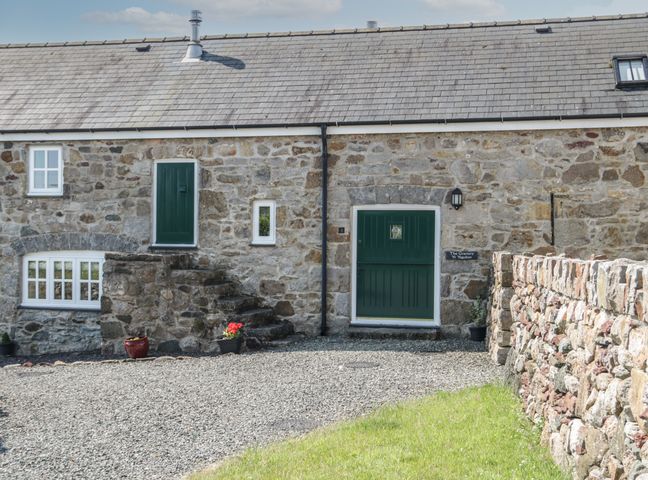 A stone house with green doors and windows with stairs and flower pots at No 1 The Granary in Capel Coch near Llannerch-Y-Medd
