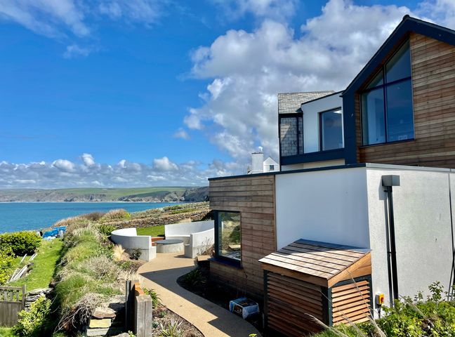 Modern house with wooden and white exterior near a coastal path and seating area overlooking the sea at The Old Coastguard Lookout in Port Isaac