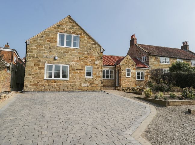 A stone house with a paved driveway and a garden with plants at Rose Cottage in Faceby near Swainby