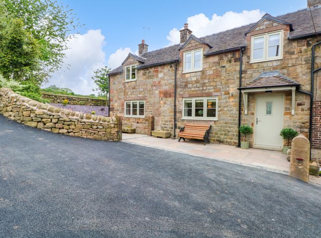 A stone cottage with windows a bench and potted plants beside the door with a stone wall and paved patio at Small Lane Cottage in Blackwood Hill near Endon