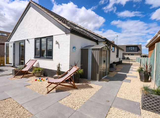 An outdoor patio area with two deck chairs beside a white wall and a shed at Waterbeach Sutton-On-Sea