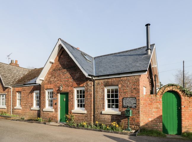 A brick house with a green door and windows and a small garden bed at Station Masters Cottage in Blakedown