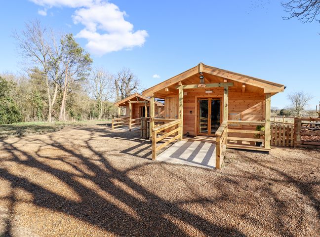 Two wooden cabins with porches on a gravel area surrounded by trees at Clover Lodge in Theberton near Leiston