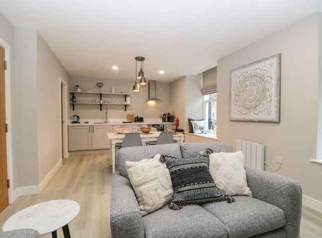 A living room with gray sofa and patterned cushions next to a dining table and kitchen area at Coniston in Kendal
