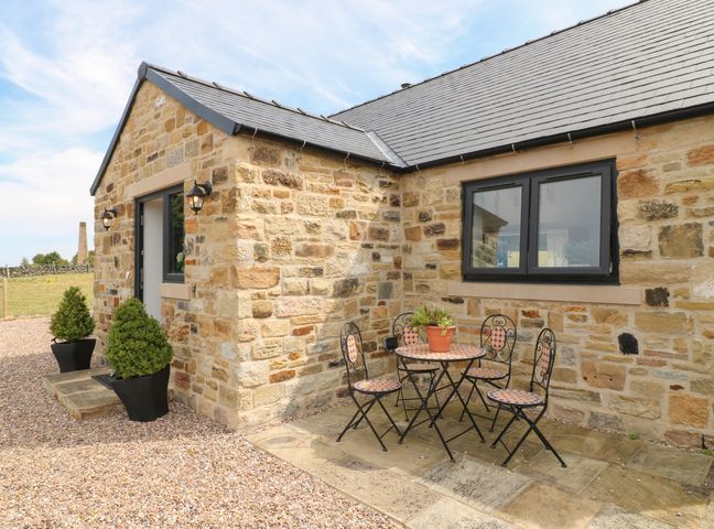 An outdoor patio with a round table and four chairs next to a stone cottage at The Cottage in Stone Edge