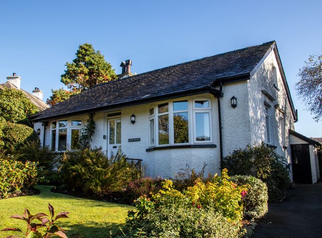 A garden and pathway in front of a white cottage with a slate roof at Curlew Cottage at Hawkshead