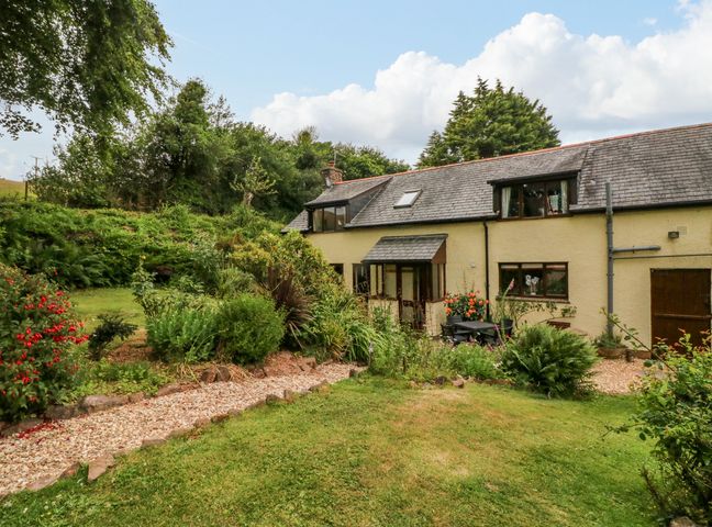 A garden with plants and a gravel path outside a yellow house with a slate roof at Elsworthy Farm Cottage in Wootton Courtenay