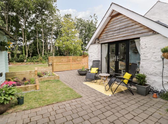 A patio with two chairs and a small table outside a white house with glass doors and raised flower beds at The Old Stable in Henryd near Conwy