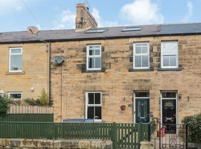 A stone terraced house with blue door and green fence at 19 Duke Street in Alnwick