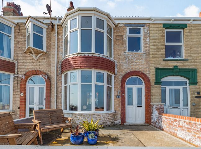 A row of brick houses with white doors and windows two wooden benches and three blue plant pots outside a house at 14 The Promenade Withernsea