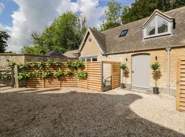 A gravel courtyard with wooden fences and potted plants outside a stone building at The Hayloft in Sherston