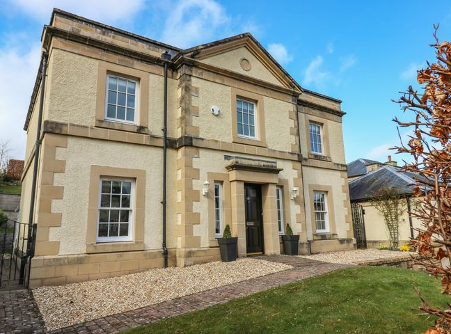 The exterior of a two-story house with a black front door windows and a small front garden at 40 Bowmont Court Heiton near Kelso