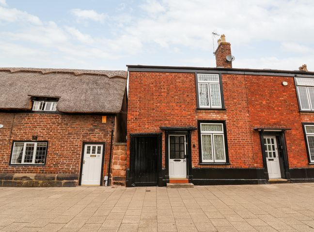 A row of brick houses with white doors and windows on a paved street at 91 Main Street in Frodsham