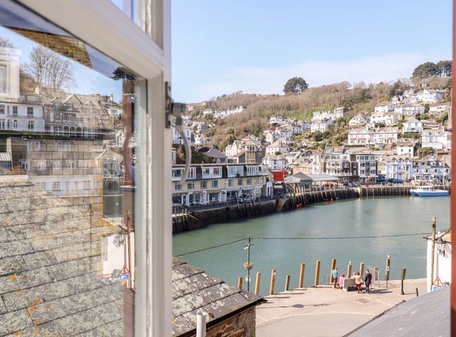 A harbor with boats houses on hillside and people near water viewed through a window at Smugglers Loft in Looe