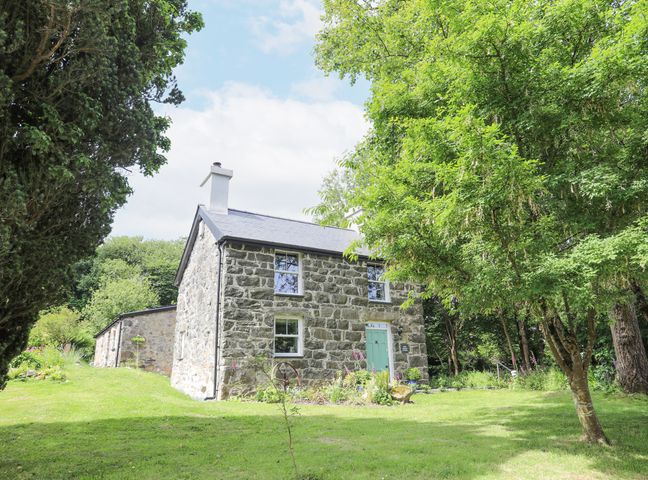Stone cottage with green door surrounded by trees and grass at Bryn Moelyn Cottage in Yr Efail near Morfa Nefyn
