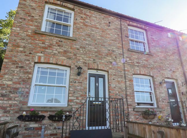 Exterior of a brick house with windows a door black railings and flower pots at Honeybee Cottage in Ripon