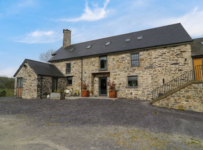 Stone house with multiple windows and a small patio at Plas Glan Yr Afon in Llangernyw