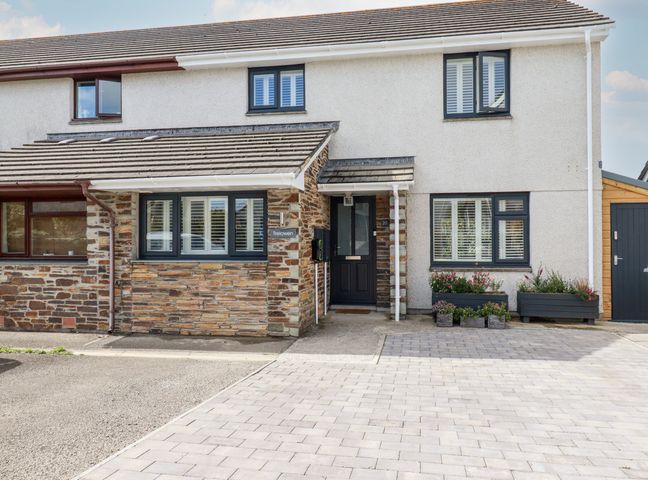 The exterior front view of a two-story semi-detached house with a paved driveway and flower planters at Trelowen in St Issey near Padstow