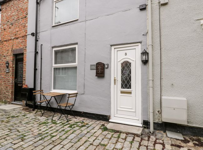 A small outdoor seating area with two wooden chairs and a table beside a white door numbered 3 on a cobblestone street at 3 Prospect Terrace Marske-By-The-Sea