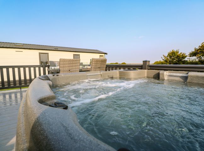 An outdoor hot tub with bubbling water next to a dining table and chairs on a deck at Chantry Lodge in Hendra Croft near Goonhavern