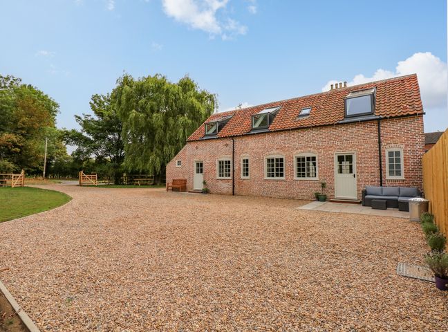 A brick house with multiple windows and doors and a gravel driveway with trees and a wooden fence at The Hayloft at Warren House in Panton near Wragby