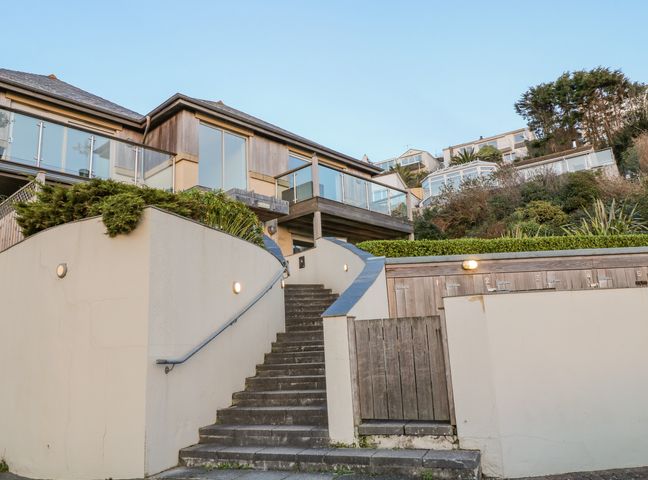 Outdoor stairs leading up to a building with large windows and glass balconies with tiled roofs and surrounding greenery at A Stone's Throw in Downderry