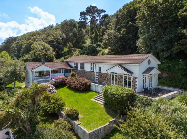A house with a garden and patio surrounded by trees at Beach Haven in Polzeath